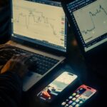 Hands typing on laptops with stock charts displayed.