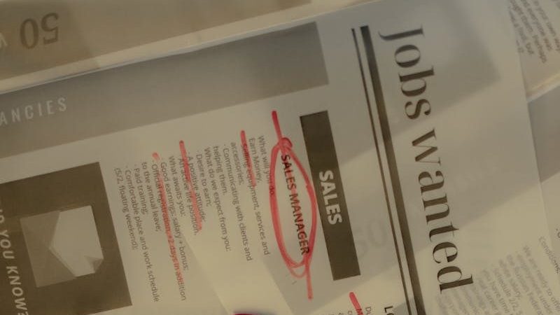 Close-up of a job search scene with a newspaper, red marker, and telephone, indicating job hunting.